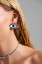Model wearing Moonveil Eye Earrings with blue eye design and silver finish