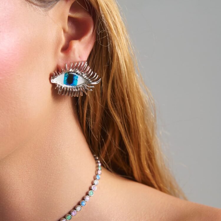 Model wearing Moonveil Eye Earrings with blue eye design and silver finish