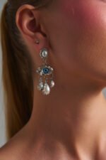 Γυναίκα που φορά τα Euphoria Eye Silver Earrings με μπλε μάτι, πέρλες και ασημί λεπτομέρειες