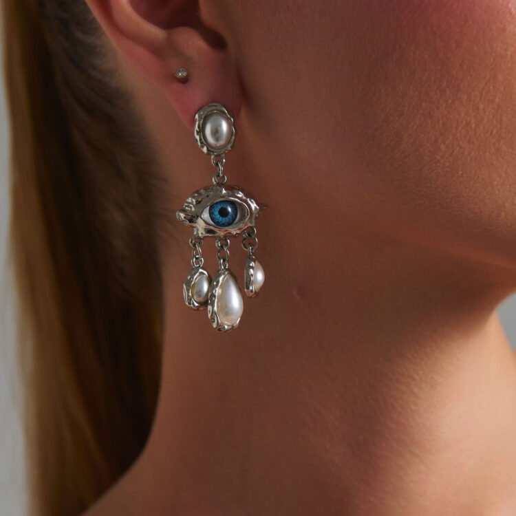 Γυναίκα που φορά τα Euphoria Eye Silver Earrings με μπλε μάτι, πέρλες και ασημί λεπτομέρειες