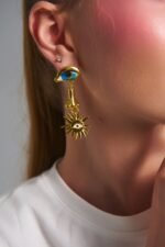 Model wearing Helios Eye Earrings with blue eye detail and gold celestial charm